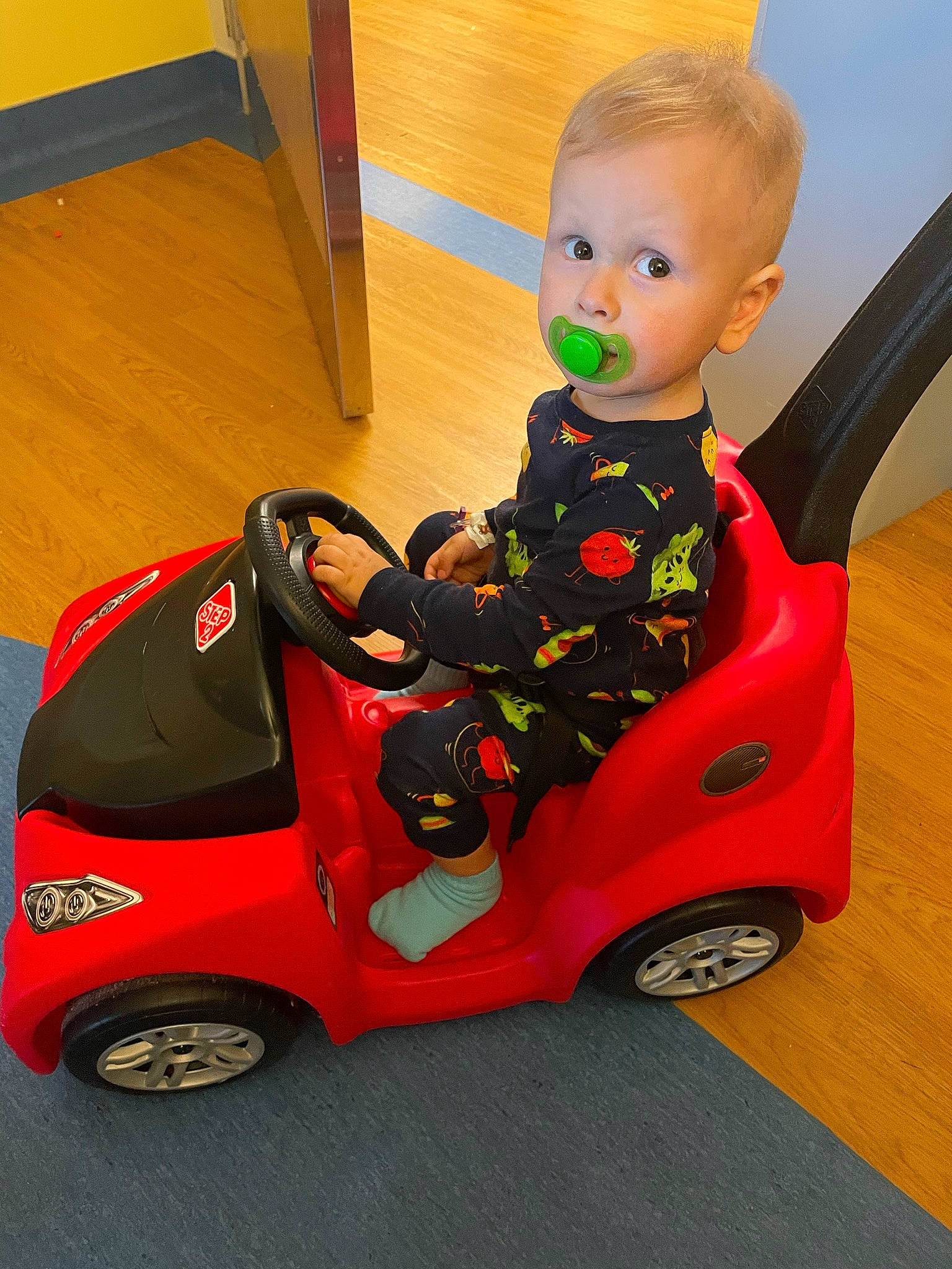 Jackson is registered to the contest to win money with this photo: automotive_design, automotive_tire, baby, baby_products, baby_toddler_clothing, car_seat, carmine, flooring, foot, human_body, human_leg, motor_vehicle, person, riding_toy, rolling, sitting, surprise, tire, toddler, toy