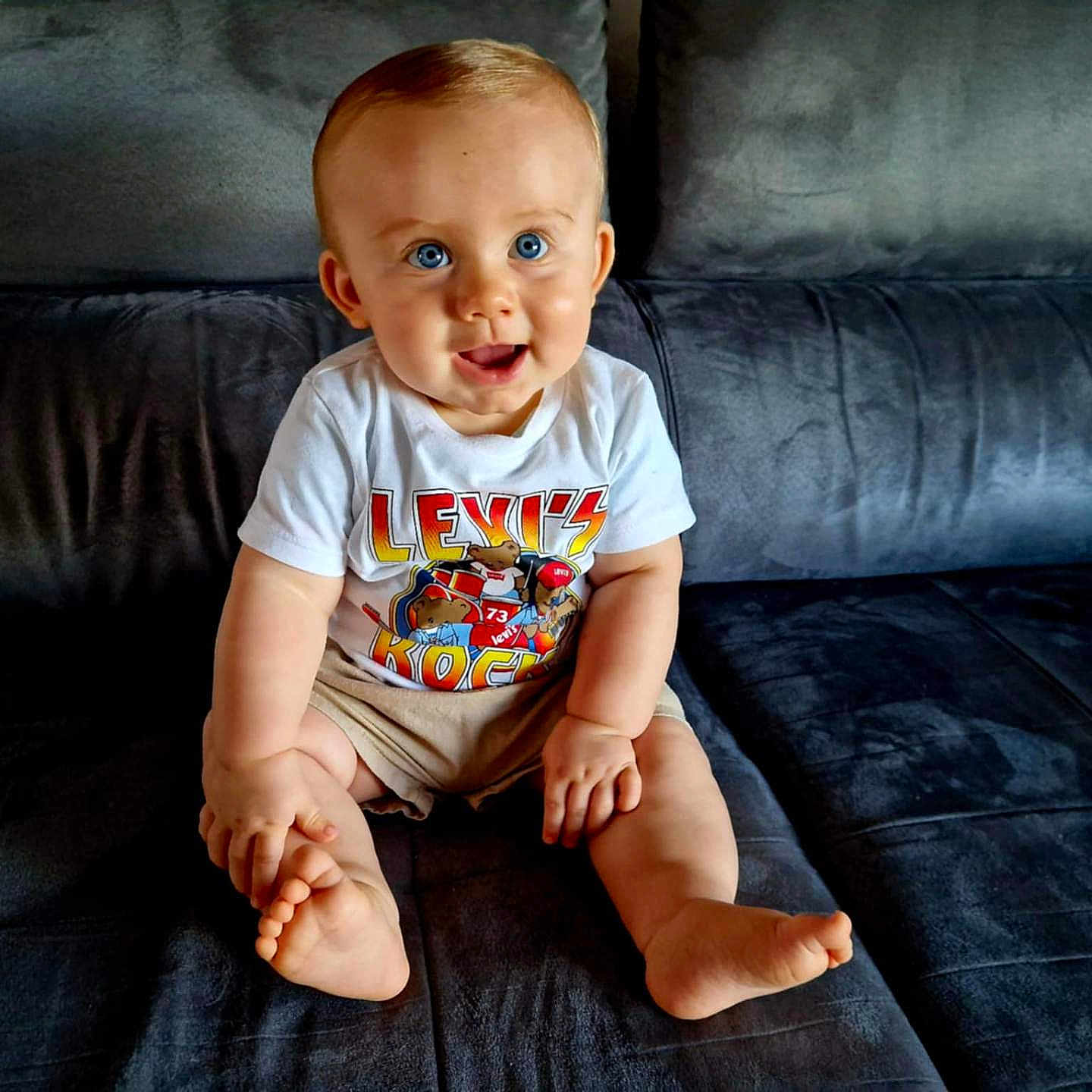 Mael participe au concours pour gagner de l'argent avec cette photo : baby, blue_eyes, child, couch, cute, feet, furniture, hands, happy, indoor, infant, legs, person, portrait, shorts, sitting, skin, smiling, tshirt, young