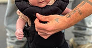 Raelynn is registered to the contest to win money with this photo: baby, infant, face, hands, tattoos, baby_carrier, person, clothing, footwear, socks, legs, outdoor, holding, closeup, cute, expression, skin, human, portrait, support