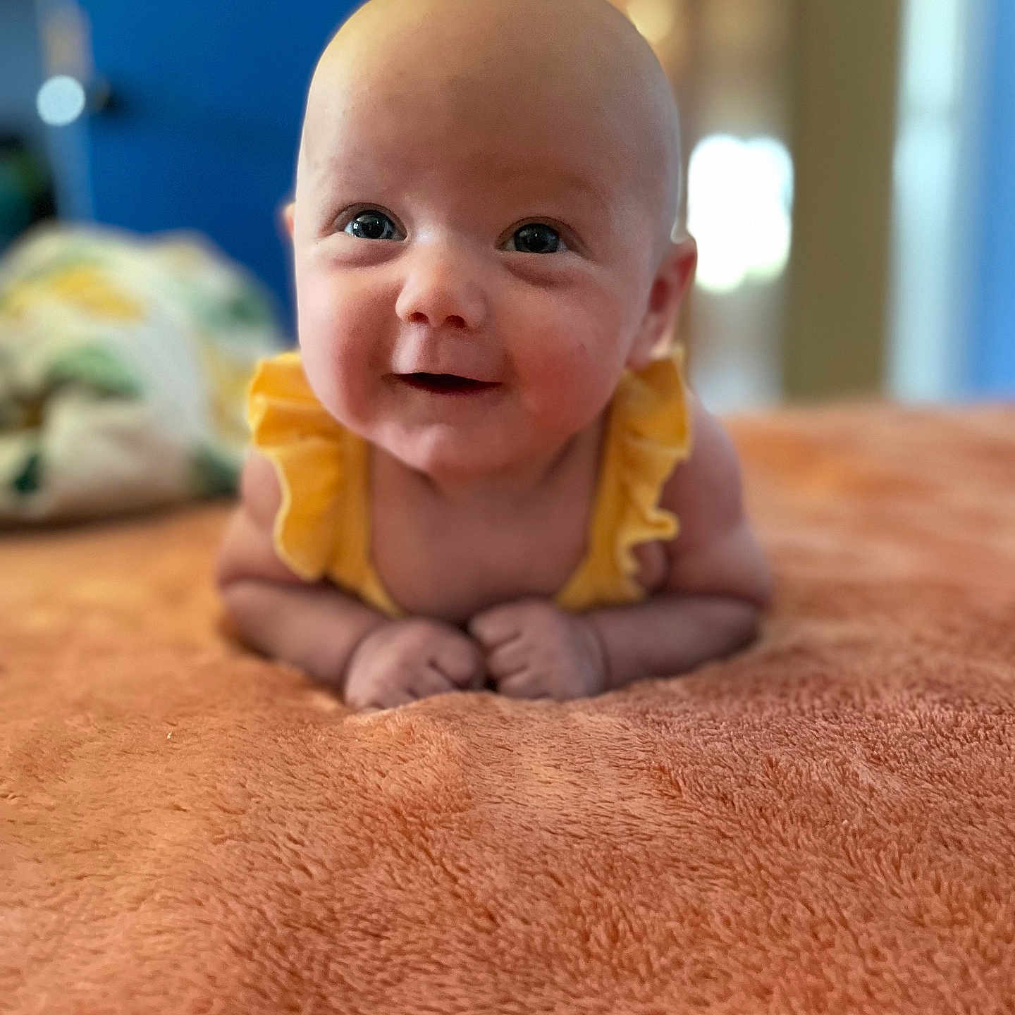 Raelynn joined the competition — help win amazing prizes! baby, infant, smiling, yellow_clothing, orange_blanket, face, eyes, skin, hands, portrait, lying_down, indoor, soft_texture, cute, happy, child, person, closeup, head, expression