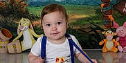 Malakai is registered to the contest to win money with this photo: baby, child, blue_rug, suspenders, white_shirt, winnie_the_pooh, tigger, piglet, rabbit, honey_pots, red_balloon, playful, smiling, indoor, portrait, cute, floor, colorful, toys, cartoon_backdrop