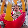 car, casual_clothing, child, curtains, cute, family, fun, furniture, home, indoor, light, living_room, man, person, plastic, playtime, smiling, sunlight, toddler, toy_car