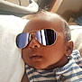 Xavier is registered to the contest to win money with this photo: baby, infant, sunglasses, striped_clothing, closeup, portrait, face, child, relaxing, indoors, soft_light, cute, young, person, fashion, accessory, head, skin, buttoned_shirt, resting