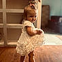 toddler, child, white_dress, barefoot, pink_bow, wooden_floor, indoor, playful, smiling, baby, person, furniture, home, portrait, cute, young_child, flooring, dress, hair_accessory, standing
