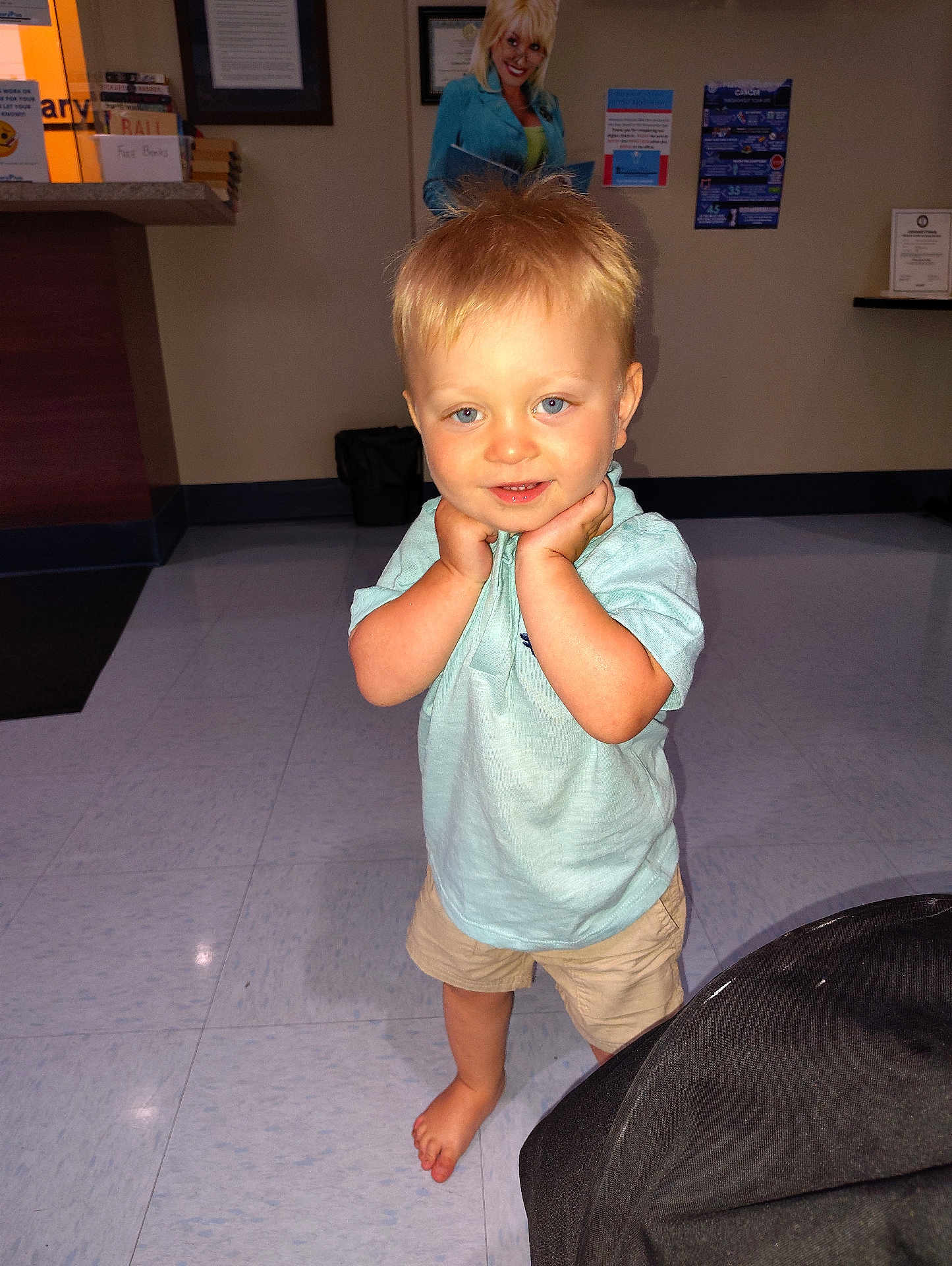 Hank is registered to the contest to win money with this photo: toddler, child, barefoot, blue_eyes, blonde_hair, shorts, polo_shirt, indoor, floor, tile_floor, posing, smiling, hands_on_face, cute, person, portrait, casual_clothing, background, cutout, photography