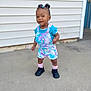 Kennedi joined the competition — help win amazing prizes! toddler, child, smiling, standing, outdoor, concrete, wall, door, tie_dye, unicorn, overalls, blue_shirt, pink_socks, black_shoes, hair_puffs, colorful_hair_ties, happy, portrait, casual_clothing, daylight
