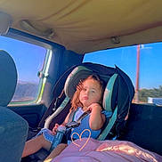 Anita is registered to the contest to win money with this photo: child, toddler, car_seat, vehicle_interior, blanket, sunlight, window, seatbelt, blue_dress, car, sitting, portrait, young_child, casual, interior, daylight, travel, seat, person, relaxed