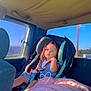 child, toddler, car_seat, vehicle_interior, blanket, sunlight, window, seatbelt, blue_dress, car, sitting, portrait, young_child, casual, interior, daylight, travel, seat, person, relaxed