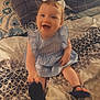 baby, child, smiling, blue_dress, bow, bed, blanket, footwear, flip_flop, happy, indoor, person, plaid_pillow, patterned_bedding, cute, portrait, sitting, young_child, home, cozy