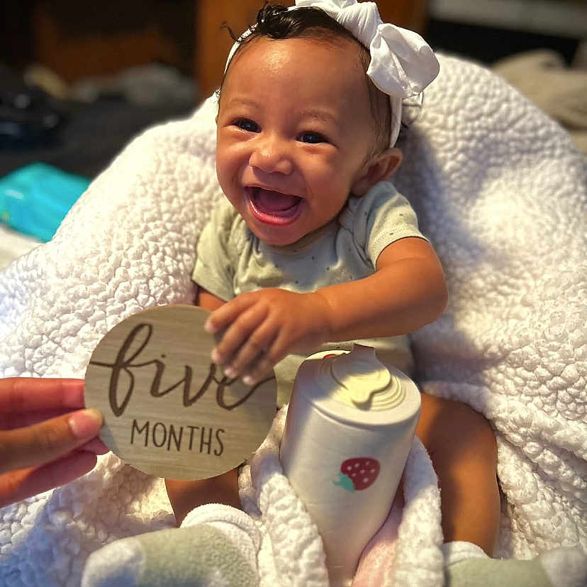 Samarianna joined the competition — help win amazing prizes! baby, bottle, bow, celebration, child, cozy, cute, five_months, hand, happy, headband, indoors, infant, milestone, person, portrait, sitting, smiling, soft_texture, white_blanket