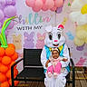 baby, child, easter_bunny, costume, balloons, bench, outdoor, decoration, carrot_balloon, flower_balloon, pastel_colors, smiling, festive, holiday, spring, headband, wooden_deck, person, happy, celebration