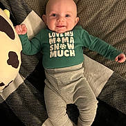 Oaklee is registered to the contest to win money with this photo: baby, infant, smile, face, eyes, clothing, green_shirt, pants, blanket, plush_toy, cow_pillow, patterned_blanket, lying_down, happy, cute, indoor, child, person, cozy, soft_toy
