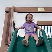 Cleo is registered to the contest to win money with this photo: casual_clothing, child, daylight, excited, expression, fun, green_slide, happy, outdoor, person, playground, playing, purple_clothing, shoes, sky, slide, smiling, toddler, wooden_structure, young_child