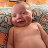 baby, smiling, infant, pillow, baseball, sports_theme, pattern, wood_floor, indoors, child, cute, happy, skin, face, head, person, closeup, comfort, soft, lying_down