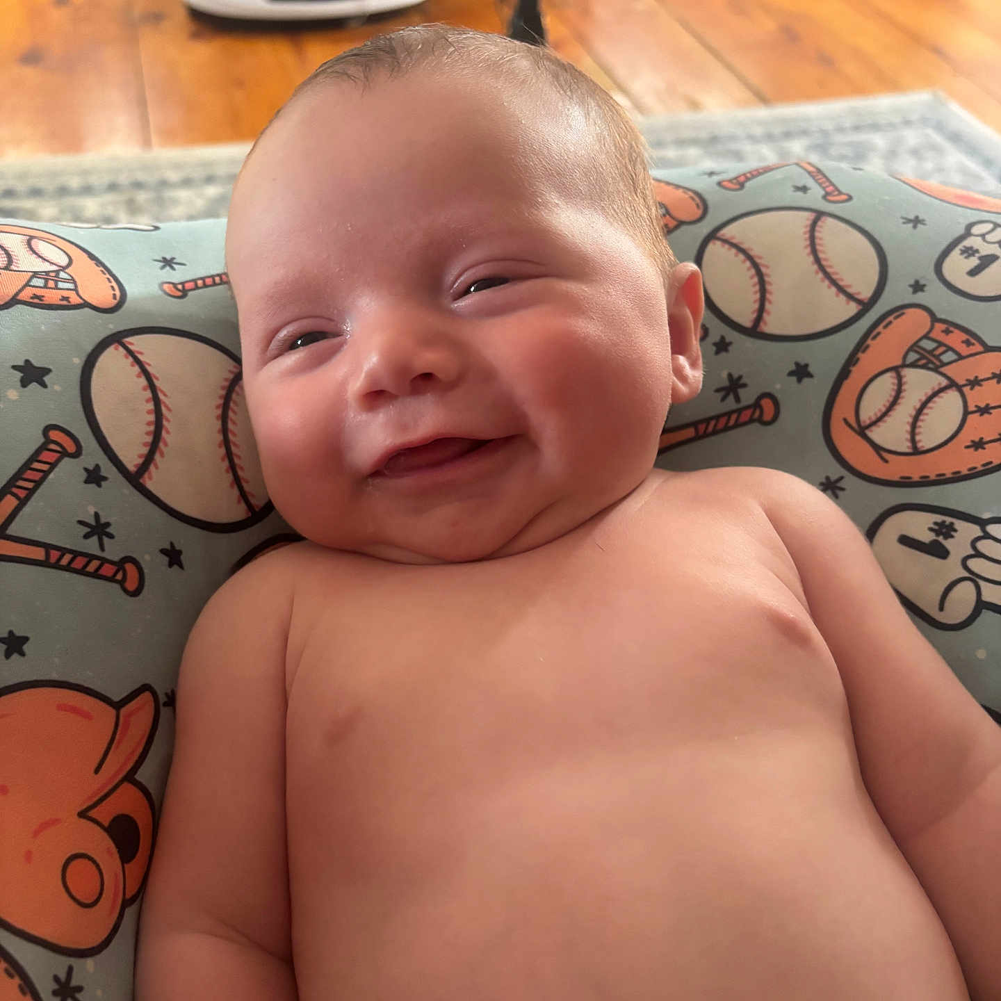 Mathew joined the competition — help win amazing prizes! baby, smiling, infant, pillow, baseball, sports_theme, pattern, wood_floor, indoors, child, cute, happy, skin, face, head, person, closeup, comfort, soft, lying_down