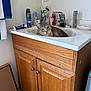 bathroom, cabinet, cat, cleaning_products, cup, curious, deodorant, domestic_cat, faucet, gray_cat, indoor, pet, relaxed, sink, soap, tile_floor, toiletries, toothbrushes, towel, wooden_cabinet