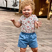 Isabella is registered to the contest to win money with this photo: toddler, child, curly_hair, smiling, outdoor, pavement, floral_shirt, blue_shorts, walking, happy, person, daylight, sunlight, cute, young_child, casual_clothing, shoes, summer, playful, nature