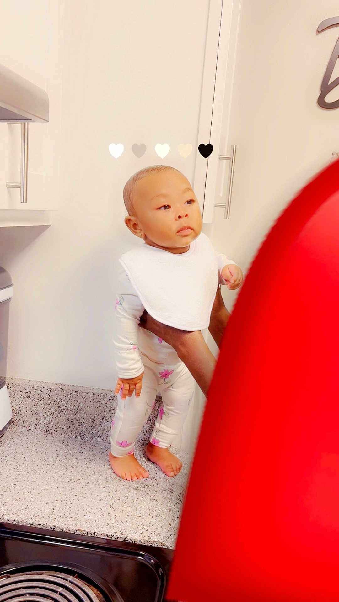 Isla is registered to the contest to win money with this photo: baby, child, toddler, kitchen, countertop, bib, pajamas, floral, barefoot, hands, adult, stove, cabinets, curious, standing, indoor, appliance, person, home, domestic