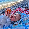 baby, child, infant, orange, hat, sunhat, quilt, blanket, beach, sea, water, pebbles, shore, blue_eyes, white_clothing, outdoor, summer, playful, cute, nature