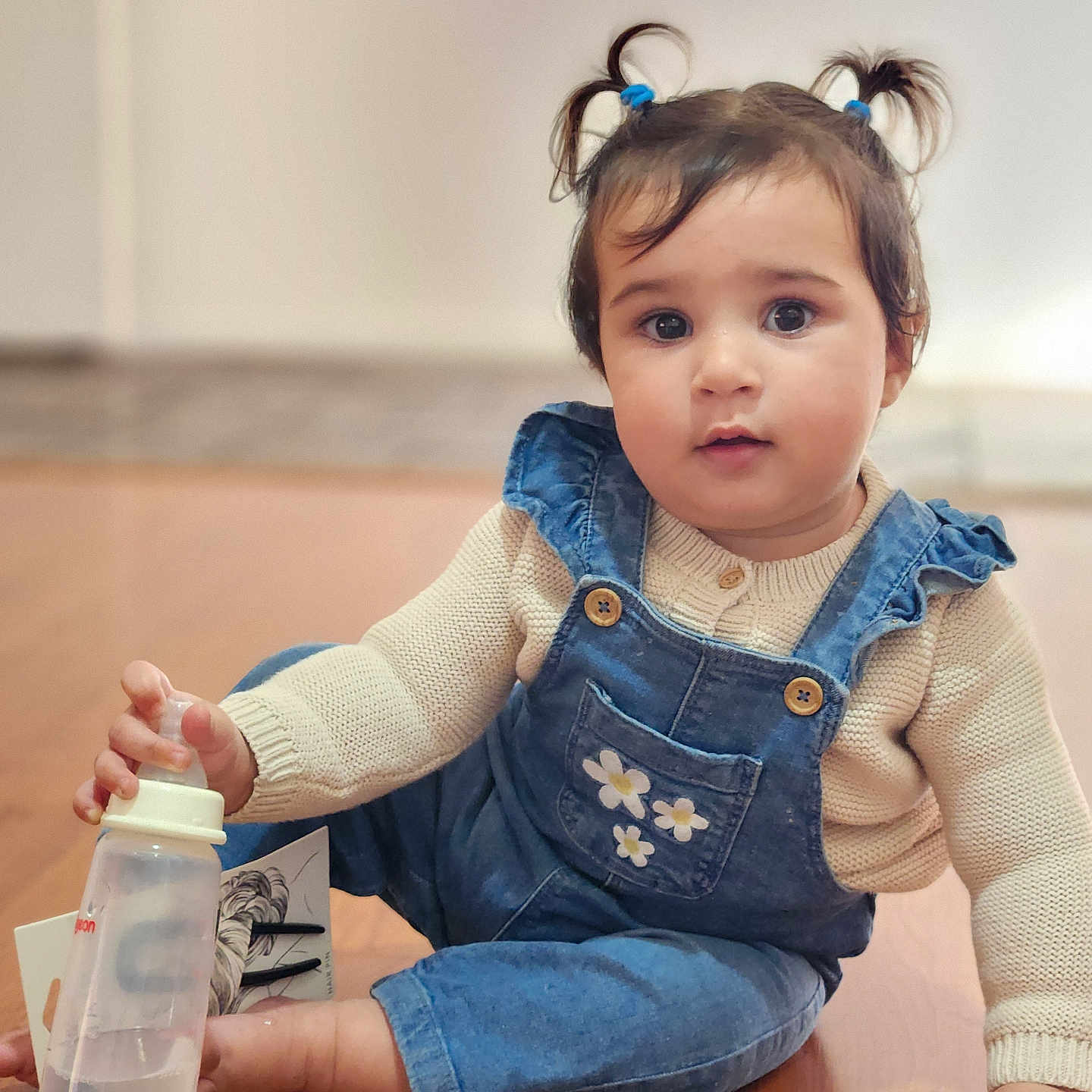 Harsimrat Chahal joined the competition — help win amazing prizes! baby, baby_bottle, casual_clothing, child, curious_expression, cute, denim_overalls, face, floor, hand, indoor, knit_sweater, natural_light, person, pigtails, portrait, sitting, toddler, wooden_floor, young_child
