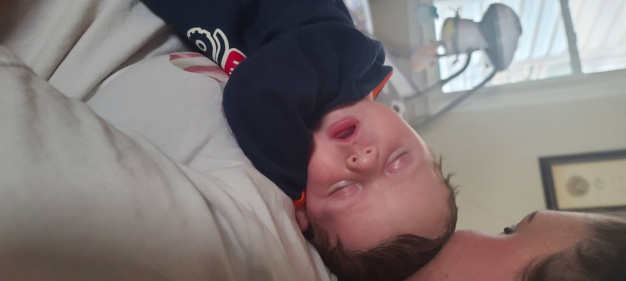 Chandler is registered to the contest to win money with this photo: abdomen, baseball_cap, bedtime, black_hair, chest, comfort, ear, elbow, eyelash, facial_hair, flesh, jaw, lip, mammal, nap, nose, person, room, sleep, toddler