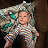 baby, blanket, casual, child, comfort, couch, cozy, curious, dinosaur_pattern, expression, face, head, home, indoor, infant, person, plush, reaching_hand, skin, striped_clothing