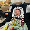 baby, blanket, car_seat, child, clothing, colorful, cozy, fabric, furniture, happy, head_support, indoor, infant, pacifier, person, poster, room, seatbelt, smile, toys