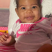 Kelani is registered to the contest to win money with this photo: baby, smiling, infant, nike, onesie, pink, unicorn, pillow, cute, happy, child, portrait, indoors, soft_toys, clothing, face, person, sitting, bright_colors, young_child