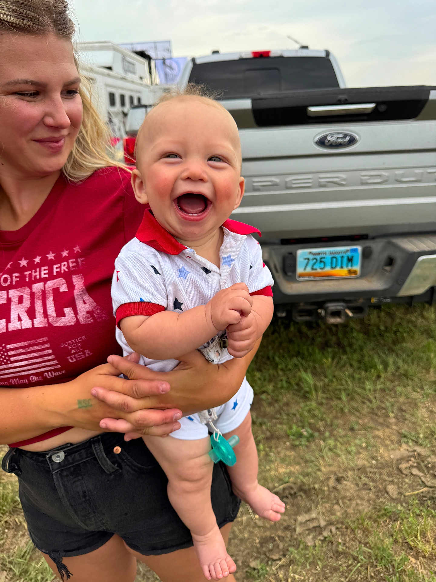 Beau joined the competition — help win amazing prizes! baby, woman, smile, happy, outdoor, grass, truck, ford, license_plate, summer, casual_clothing, holding, child, red_shirt, shorts, pacifier, blue_eyes, light_hair, cheerful, daylight