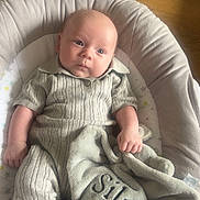 Silas joined the competition — help win amazing prizes! baby, infant, blanket, knitted_clothing, cushion, soft_toy, face, feet, hand, indoor, wooden_floor, comfort, relaxed, portrait, child, newborn, seat, plush, cozy, home