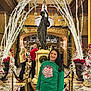 child, girl, smiling, indoor, christmas, holiday_decor, lights, statue, chandelier, festive, green_sweater, people, floor_tiles, railing, gold_decor, white_lights, poinsettia, holiday_season, portrait, museum