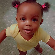 Sevyn is registered to the contest to win money with this photo: baby, barefoot, bathroom, child, curly_hair, cute, expression, floor_tiles, hair_clips, happy, indoor, looking_up, person, portrait, skin, smiling, standing, toddler, yellow_onesie, young_child