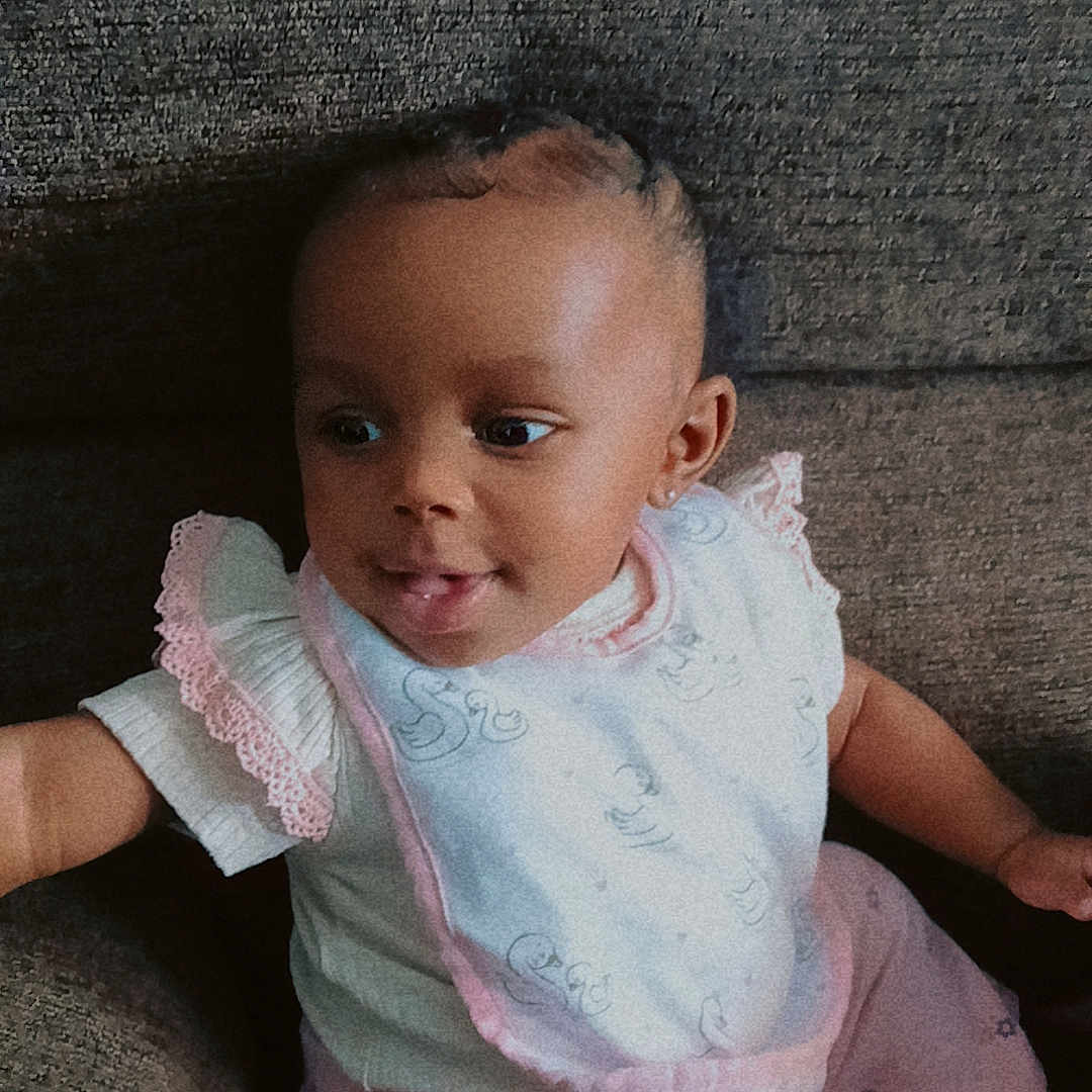 Sevyn joined the competition — help win amazing prizes! baby, bib, child, clothing, couch, cute, expression, fabric, furniture, girl, happy, indoor, infant, pink, playful, portrait, sitting, smile, white, young