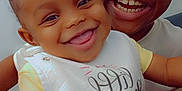 Sevyn is registered to the contest to win money with this photo: arm, baby, background, bib, child, cute, expression, face, hair_ties, hand, happy, indoor, joyful, person, portrait, sitting, skin, smiling, teeth, yellow_clothing