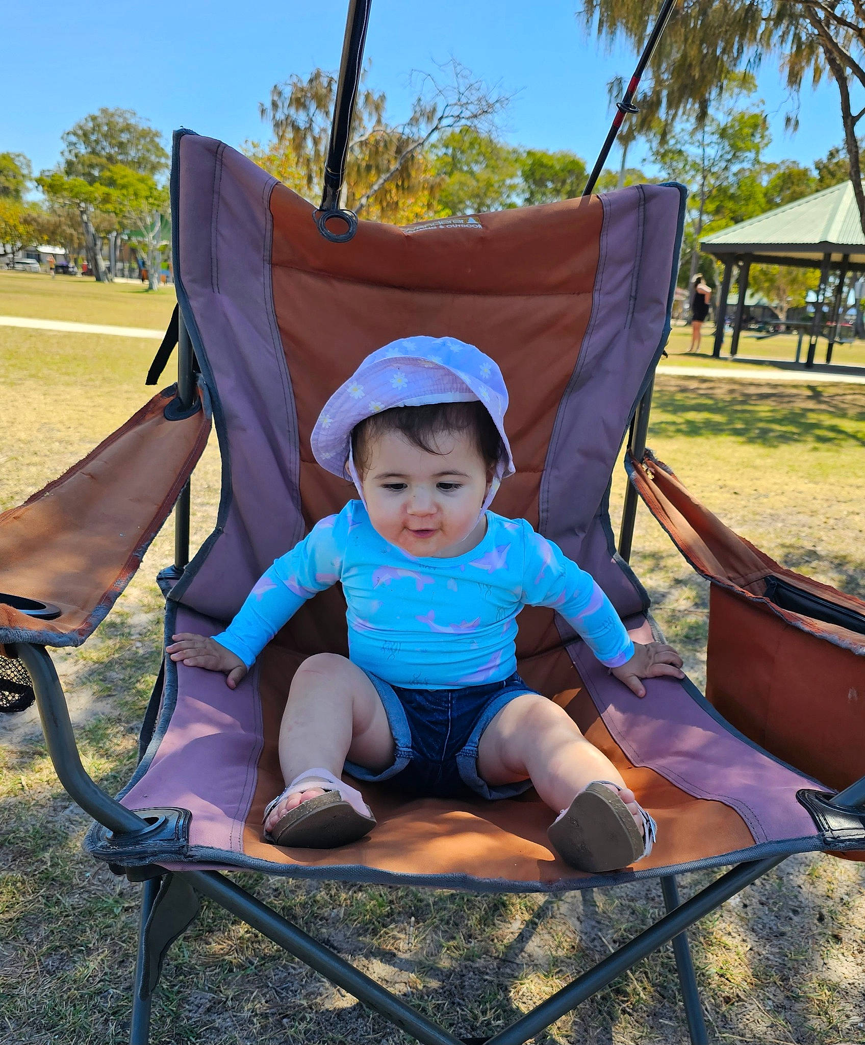 Maya is registered to the contest to win money with this photo: chair, comfort, electric_blue, fashion_accessory, fun, grass, leaf, leisure, morning, nature, outdoor_furniture, person, plant, recreation, shade, shorts, sitting, sky, tints_and_shades, toddler