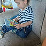 Gaspard a rejoint le concours — aidez-le/la à gagner de superbes lots ! child, toddler, striped_shirt, book, reading, couch, indoor, sitting, blue_jeans, shoes, pillow, bag, curly_hair, casual_clothing, person, home, furniture, relaxed, focused, young