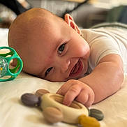 Eliott participe au concours pour gagner de l'argent avec cette photo : baby, smiling, toy, infant, happy, hand, face, lying_down, cute, child, skin, indoor, playing, closeup, expression, cheerful, young, person, head, furniture