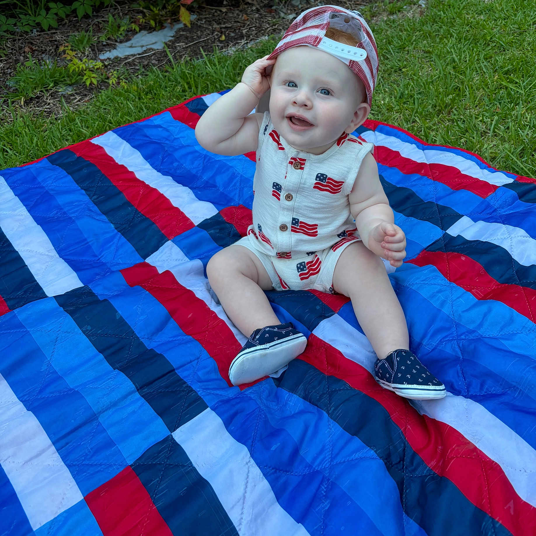 Liam is registered to the contest to win money with this photo: baby, child, outdoor, grass, blanket, cap, hat, shoes, smile, happy, blue_eyes, sitting, cute, infant, playful, summer, casual_clothing, portrait, colorful, daylight