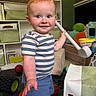 toddler, child, toy, indoor, playroom, golf_club, smiling, shorts, striped_shirt, red_hair, blue_eyes, storage_bins, basketball, baseball, plush_toys, furniture, carpet, happy, person, portrait