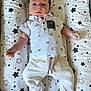 baby, infant, child, shirt, pants, sock, star_pattern, cushion, lying_down, cute, face, hair, white_clothing, beige_clothing, patterned_clothing, baby_bedding, comfortable, indoors, portrait, young_child
