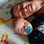 baby, adult, pacifier, playmat, animal_pattern, christmas_sweater, blue_eyes, smile, face, lying_down, indoor, child, person, head, closeup, skin, hair, cute, comfort, family