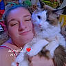 person, cat, stuffed_animals, selfie, hugging, indoor, smiling, plush_toys, red_clothing, face, pet, feline, cozy, cute, long_hair, relaxed, close_up, home, comfort, affection