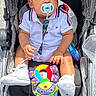 Taevon is registered to the contest to win money with this photo: baby, child, stroller, pacifier, toy, white_shoes, polo_shirt, infant, outdoor, daylight, colorful_toy, seat, cute, small_hands, baby_clothing, fabric, footwear, person, portrait, casual