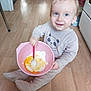 baby, blue_eyes, bowl, child, clothing, cooking, cute, floor, food, home, indoor, kitchen, light_hair, mixing, onesie, panda, smiling, spoon, toddler, wooden_floor
