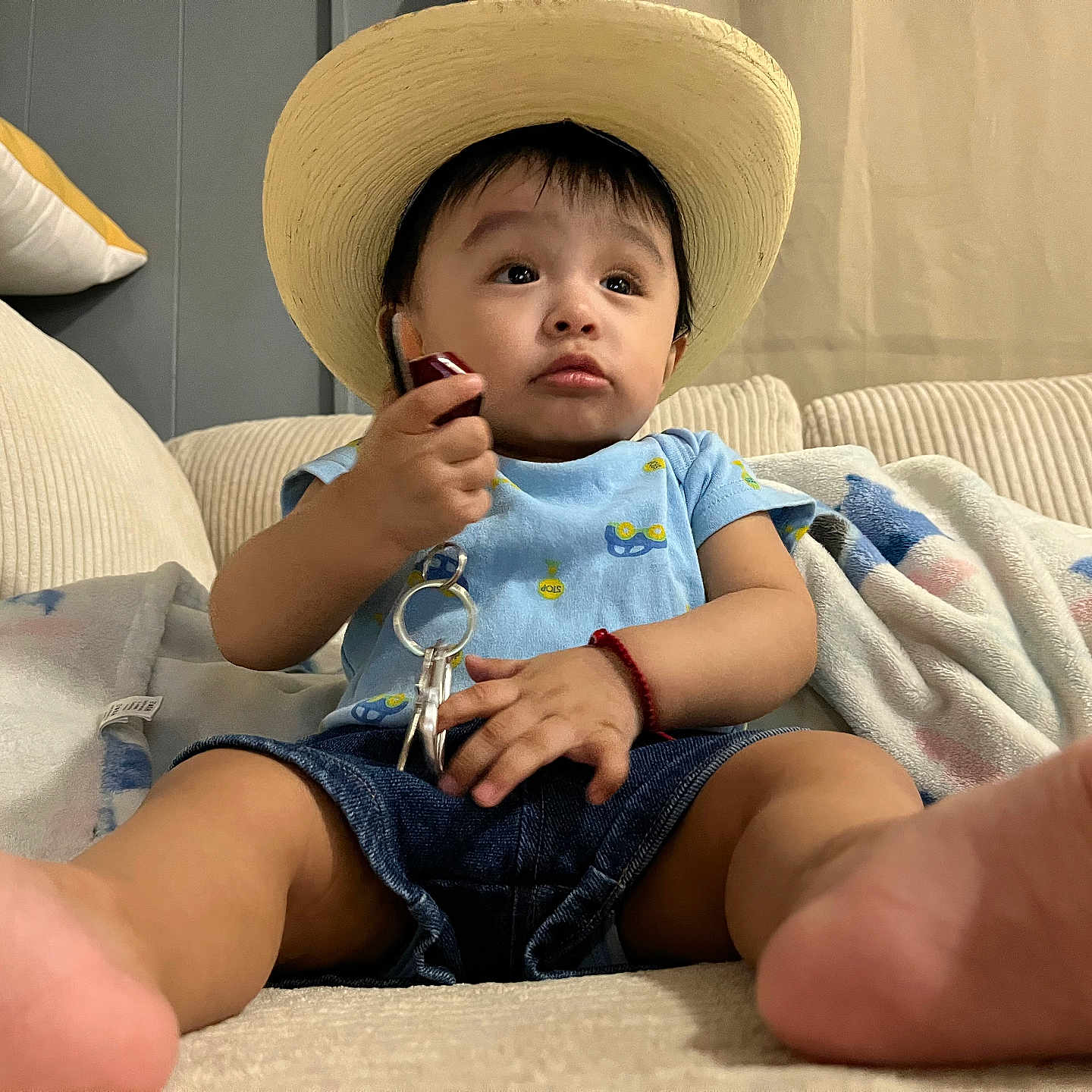 Levy is registered to the contest to win money with this photo: baby, blanket, bodypart, clothing, couch, eating, electronics, face, finger, furniture, hand, handcuffs, hat, head, mobilephone, pants, person, phone, sitting, sunhat