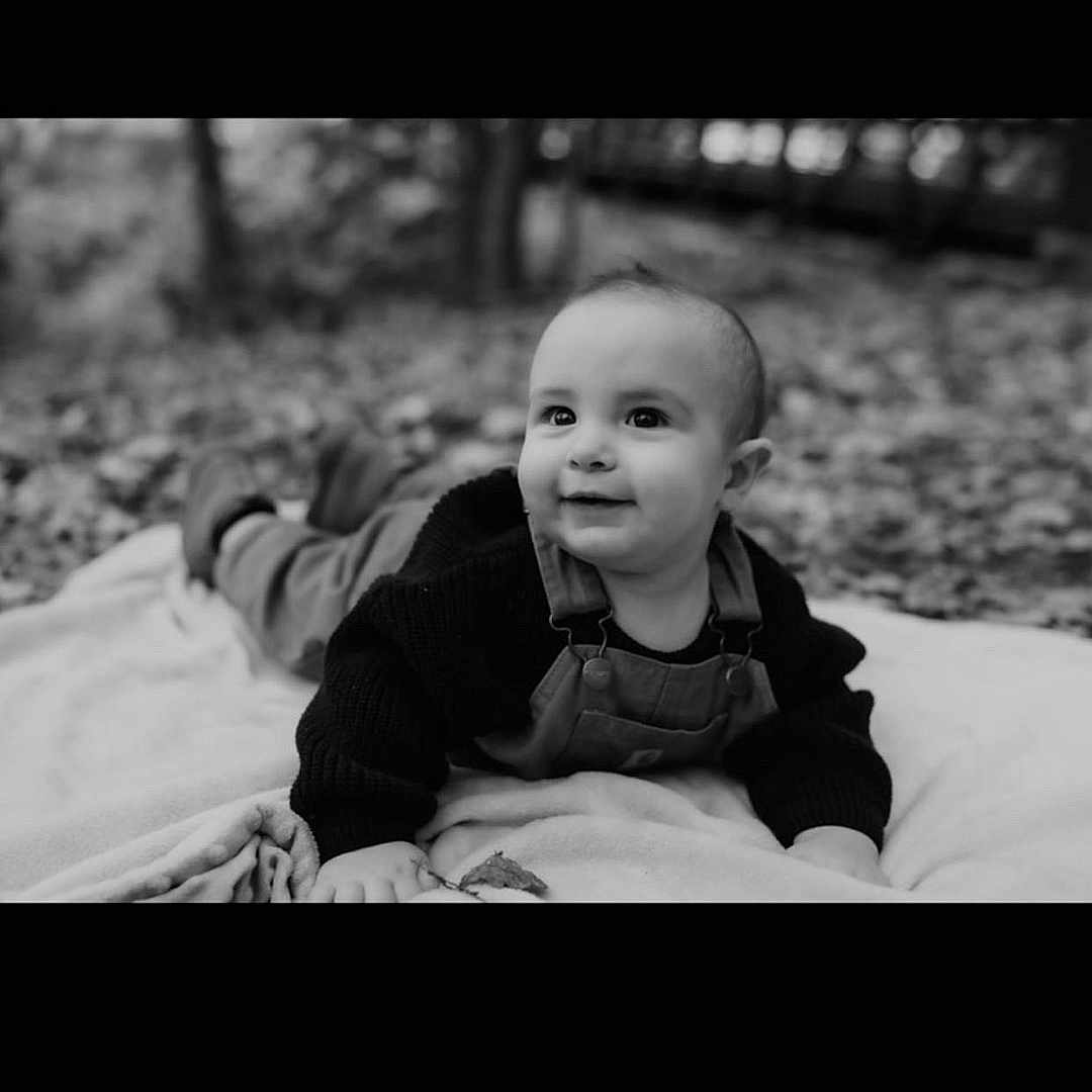 Hunter is registered to the contest to win money with this photo: baby, bodypart, clothing, coat, face, finger, hand, happy, head, jacket, laughing, mouth, outdoors, pants, person, photography, portrait, sitting, smile, teeth