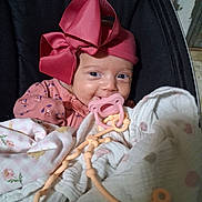 Olivia joined the competition — help win amazing prizes! baby, infant, child, portrait, smiling, pacifier, pink_bow, headband, blanket, swaddled, floral_clothing, pink_clothing, cozy, indoor, seated, close_up, face, blue_eyes, toy, nursery