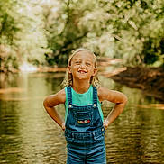 Zoey is registered to the contest to win money with this photo: child, girl, smiling, portrait, outdoors, woodland, forest, stream, water, nature, sunlight, summer, overalls, denim, turquoise_shirt, blonde_hair, standing, hands_on_hips, reflection, bokeh