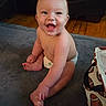 baby, child, smiling, happy, sitting, diaper, indoor, floor, rug, bag, football_pattern, cute, infant, skin, face, hand, foot, wooden_floor, couch, expression