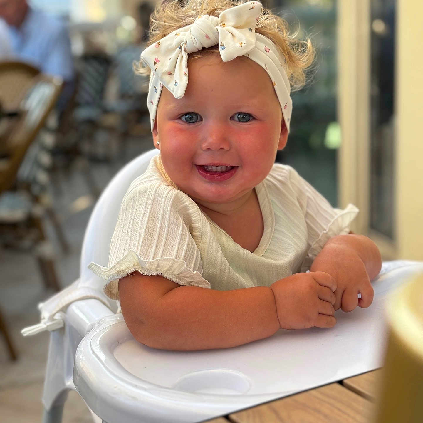 Aleya participe au concours pour gagner de l'argent avec cette photo : baby, blush, cafe, child, curly_hair, cute, face, furniture, happy, headband, high_chair, indoor, person, portrait, seat, skin, smiling, table, toddler, white_clothing